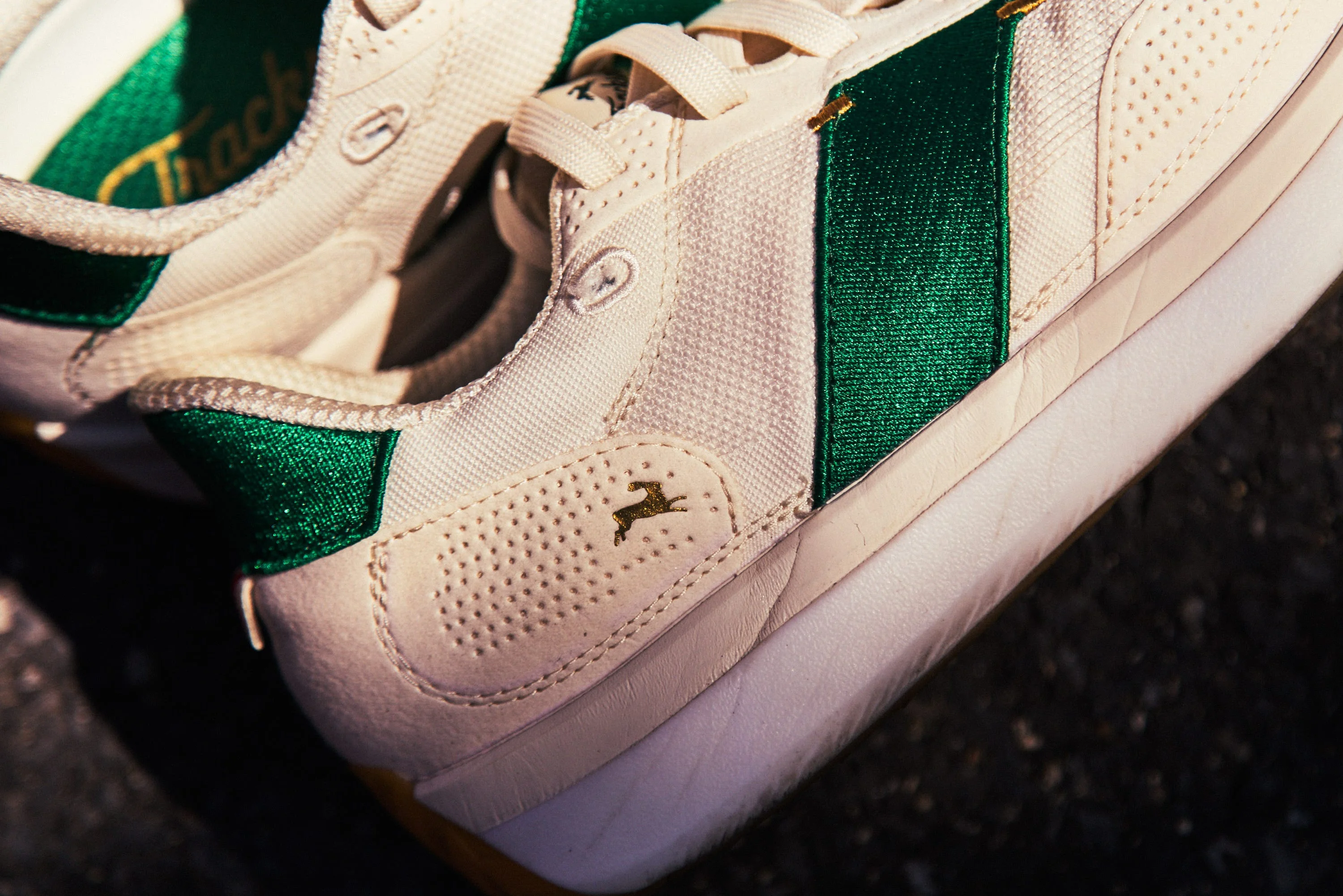Close-up of a stylish white sneaker with green accents and a textured finish.