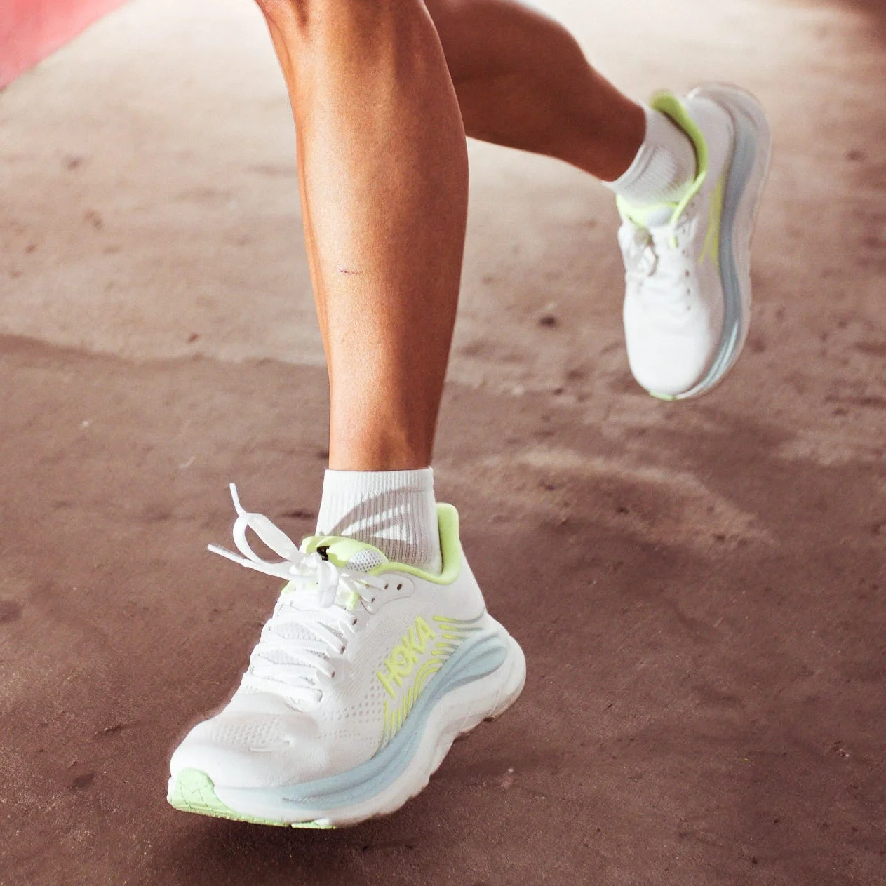 A person running in a green outfit and white sneakers on a concrete surface near a red wall.