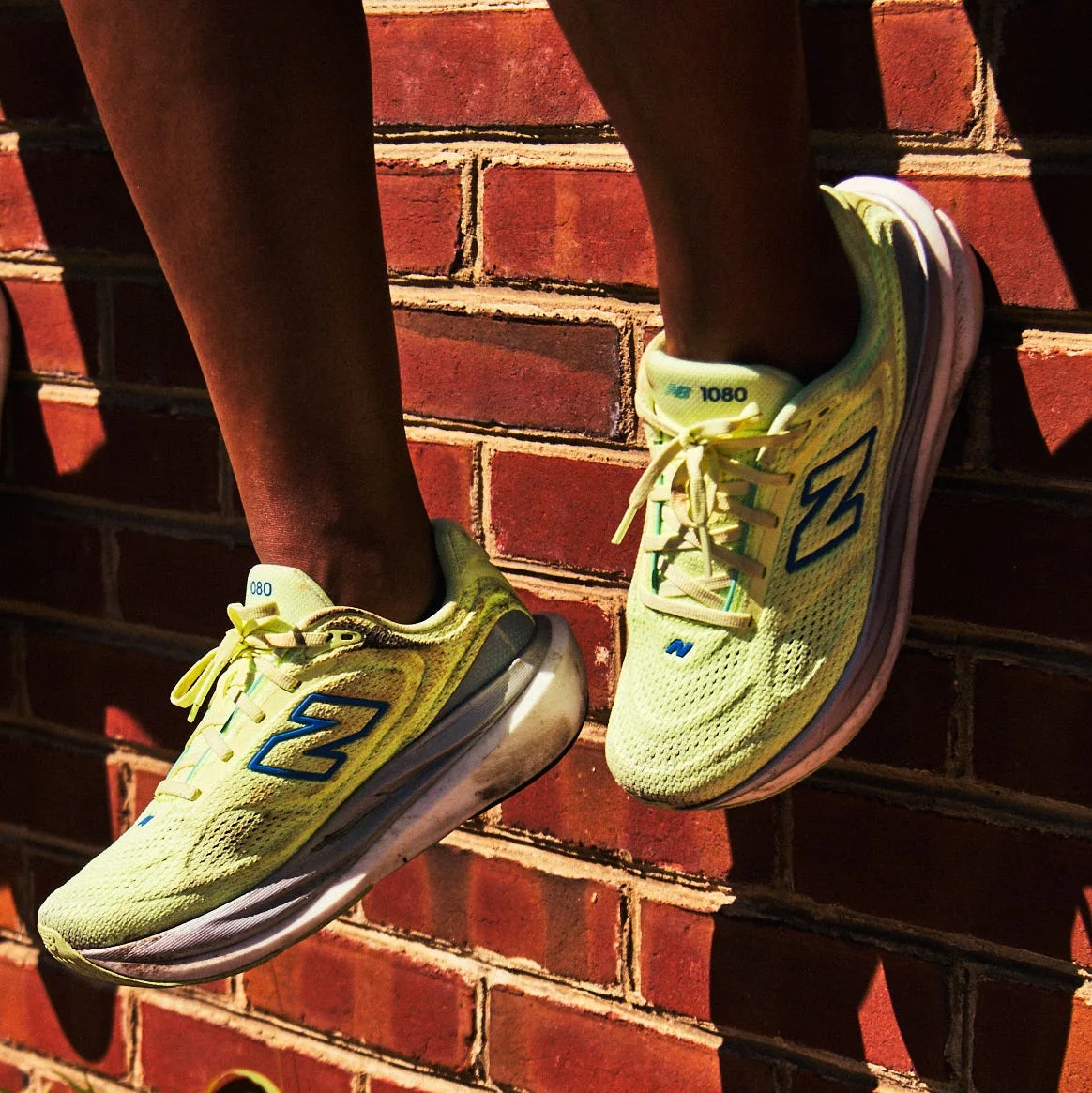 Close-up of vibrant yellow sneakers against a brick wall, with sunlight casting shadows during an active moment.