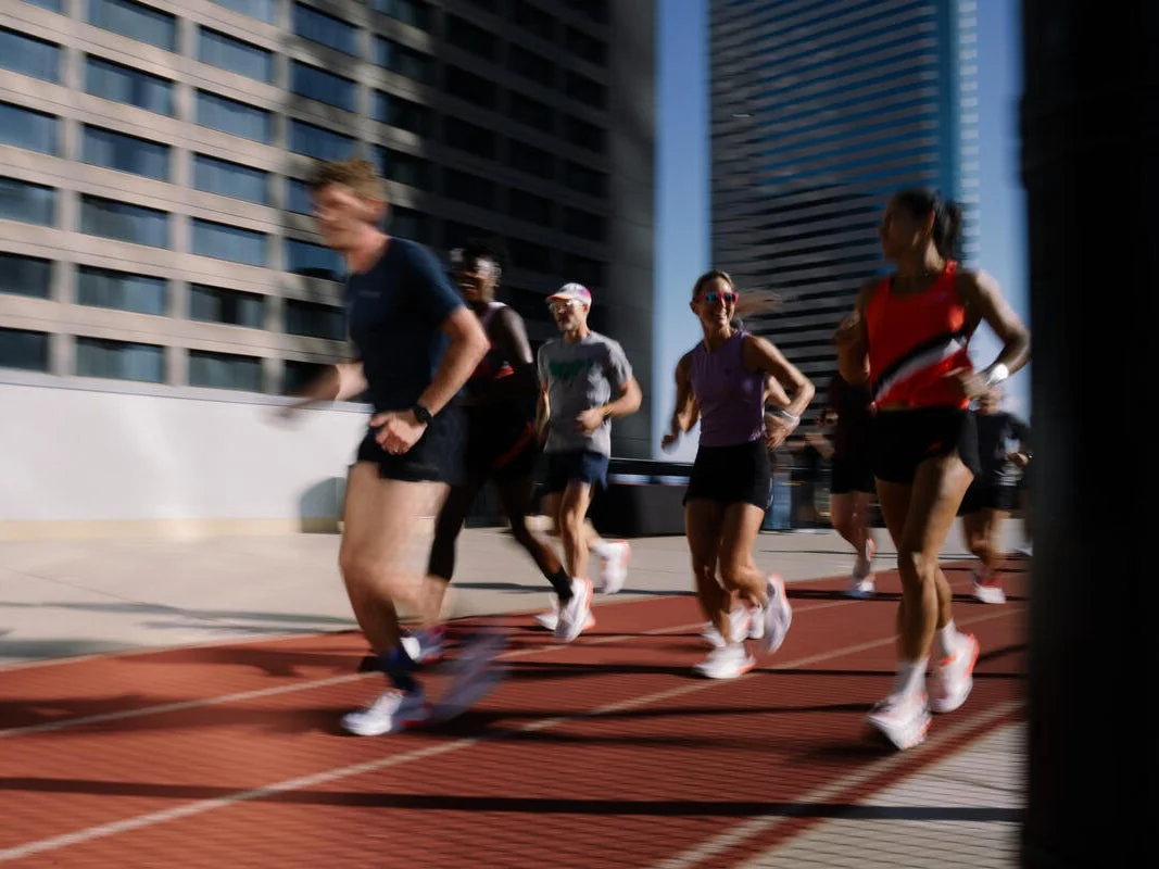 Group of runners training on an outdoor track with tall buildings in the background.