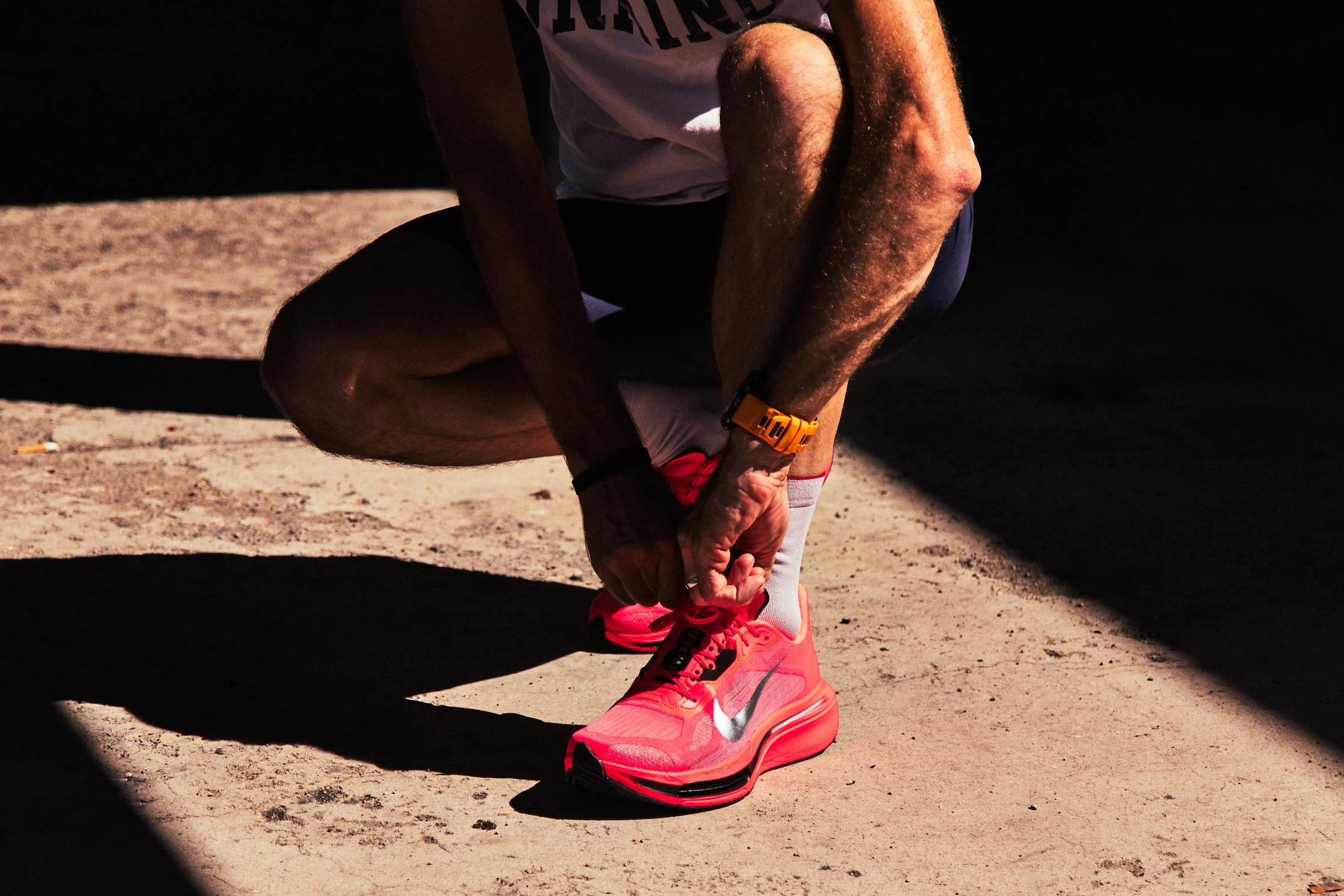 A person tying bright pink athletic shoes while kneeling on a concrete surface.