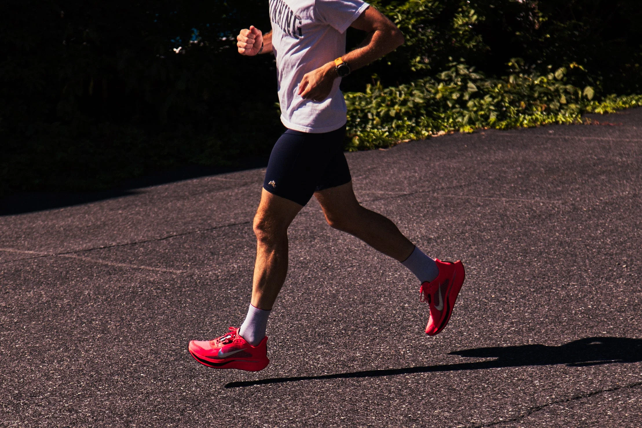 A person jogging on a paved surface, wearing a white shirt, black shorts, and bright pink running shoes.