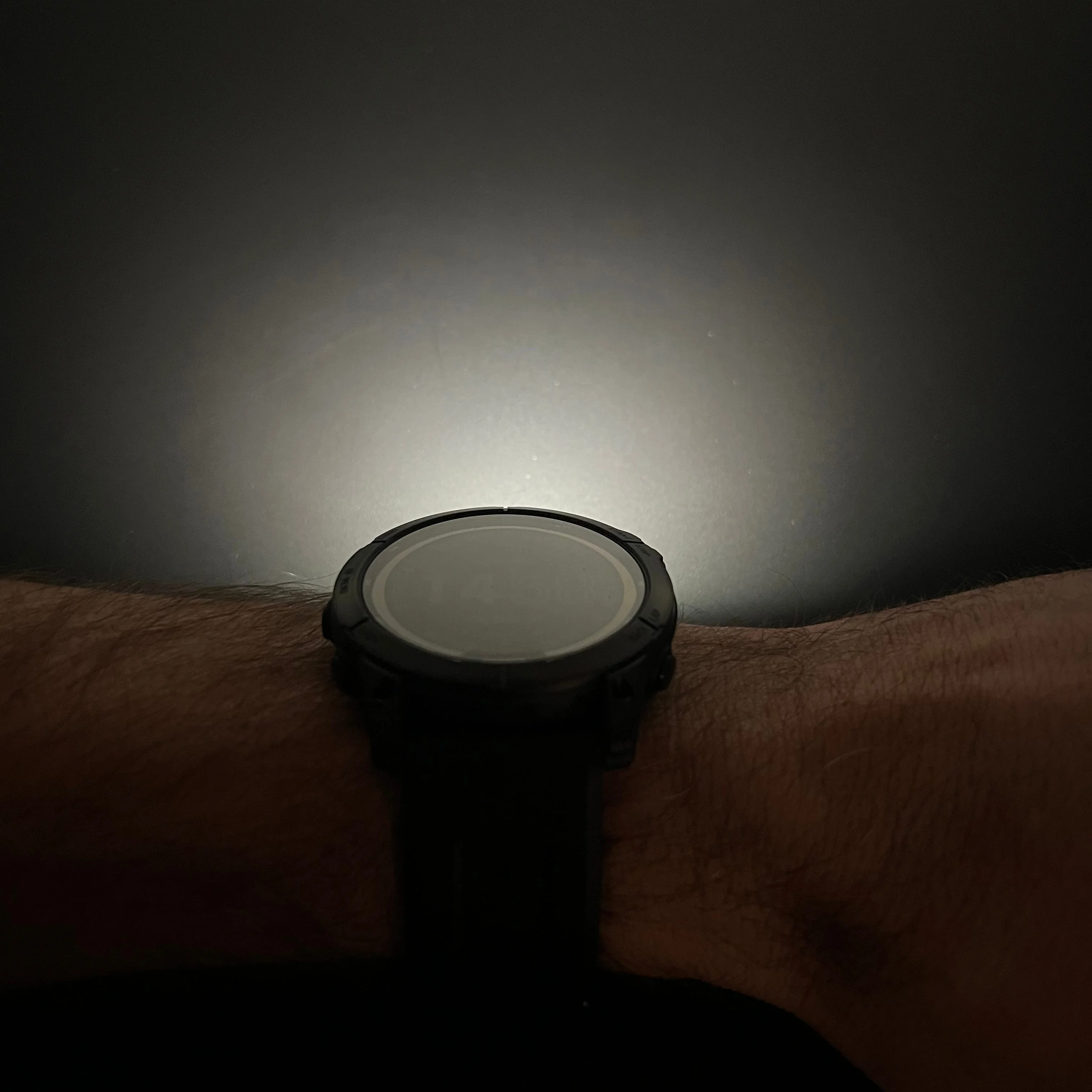 A black smartwatch resting on a wrist with a faint light glow behind it.