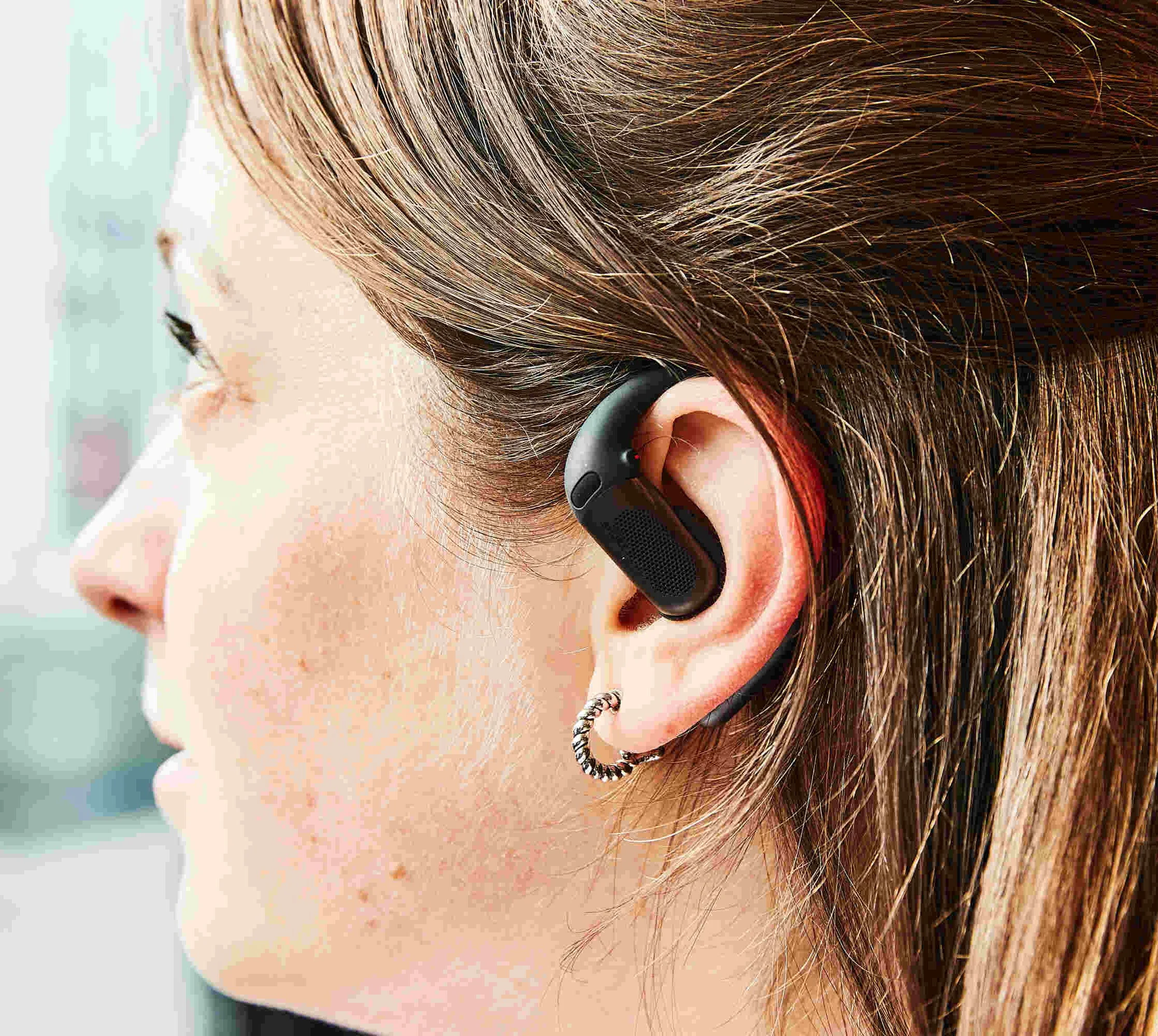 A woman with long hair wearing wireless earbuds, seen from the side.