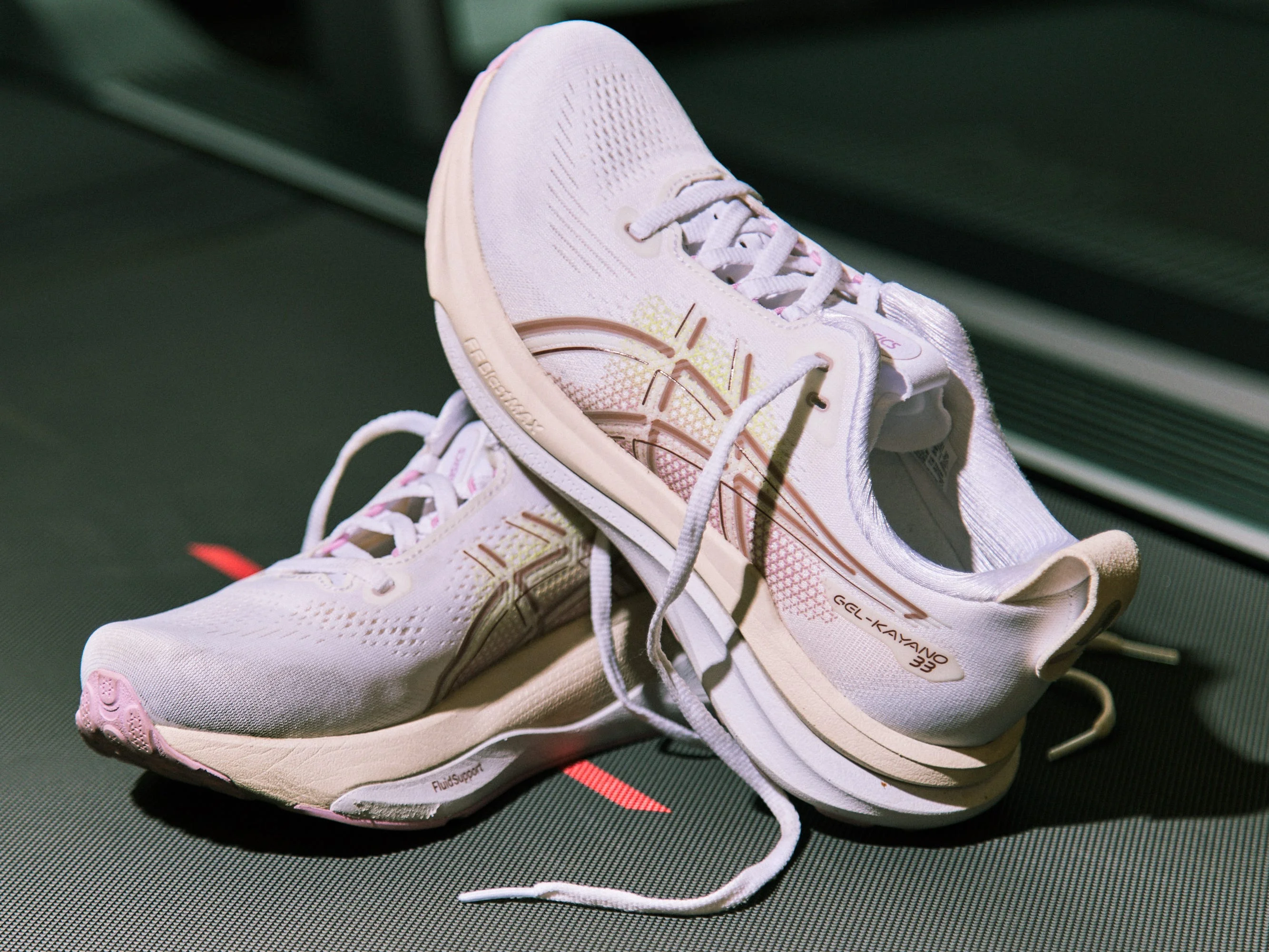 Pair of Asics Gel Kayano 33 shoes with soft pink accents on a dark background. Pair of Asics Gel Kayano 33 shoes with soft pink accents on a dark background.