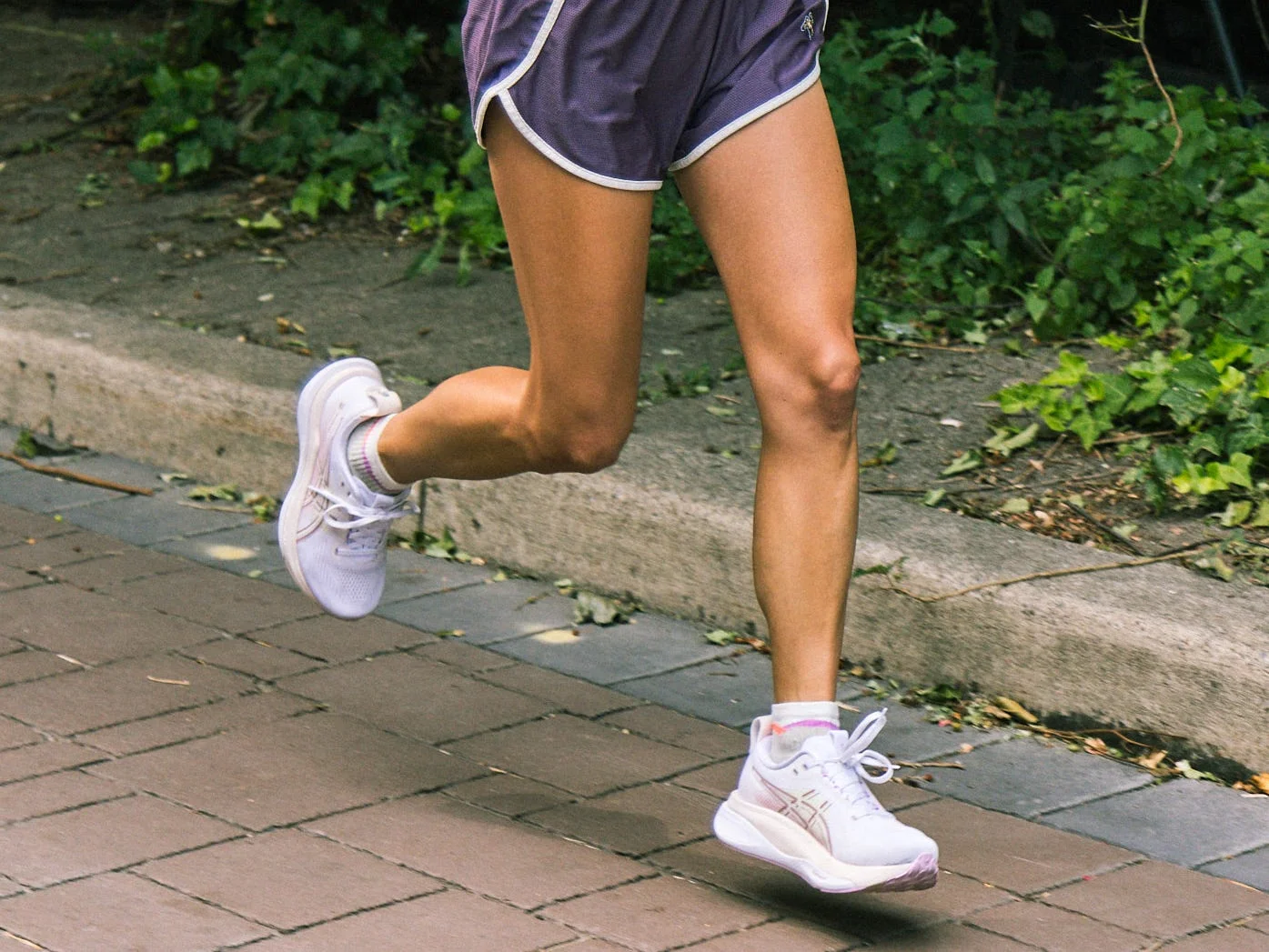 A woman with tattoos running outdoors in athletic wear on a sunny day along a leafy path. A woman with tattoos running outdoors in athletic wear on a sunny day along a leafy path.