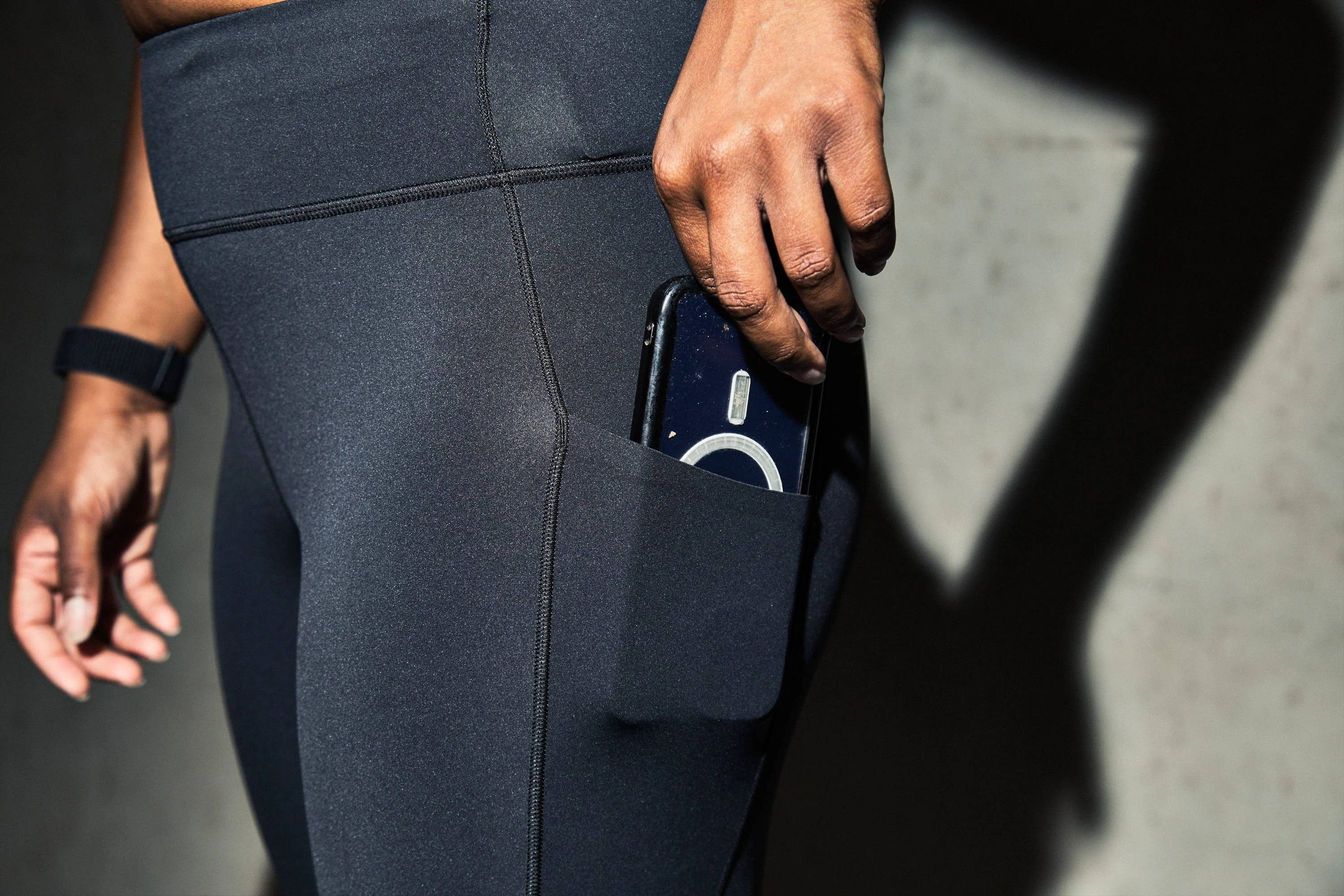 A person holding a phone partially visible in the pocket of black athletic leggings. A person holding a phone partially visible in the pocket of black athletic leggings.