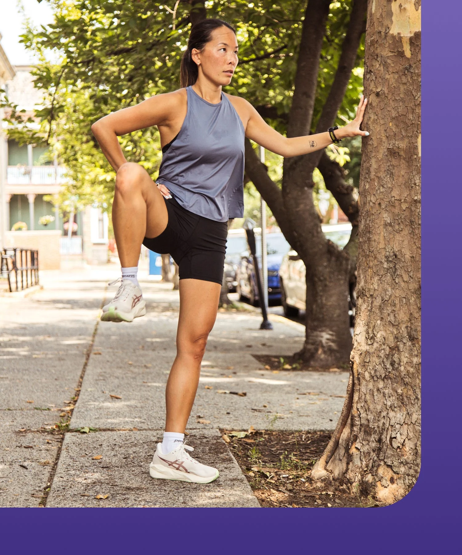 A person stretching their leg against a tree on a sunny sidewalk.