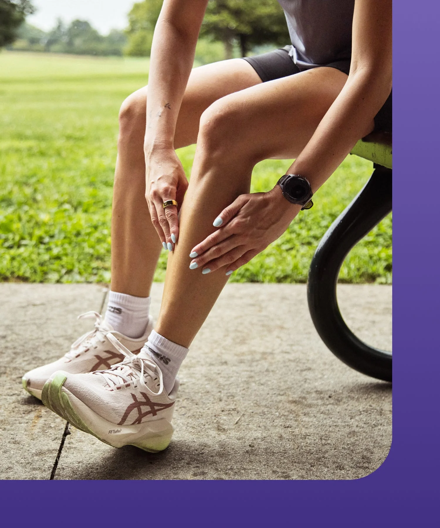 A person stretching their leg outdoors while sitting on a bench, wearing athletic shoes and shorts.