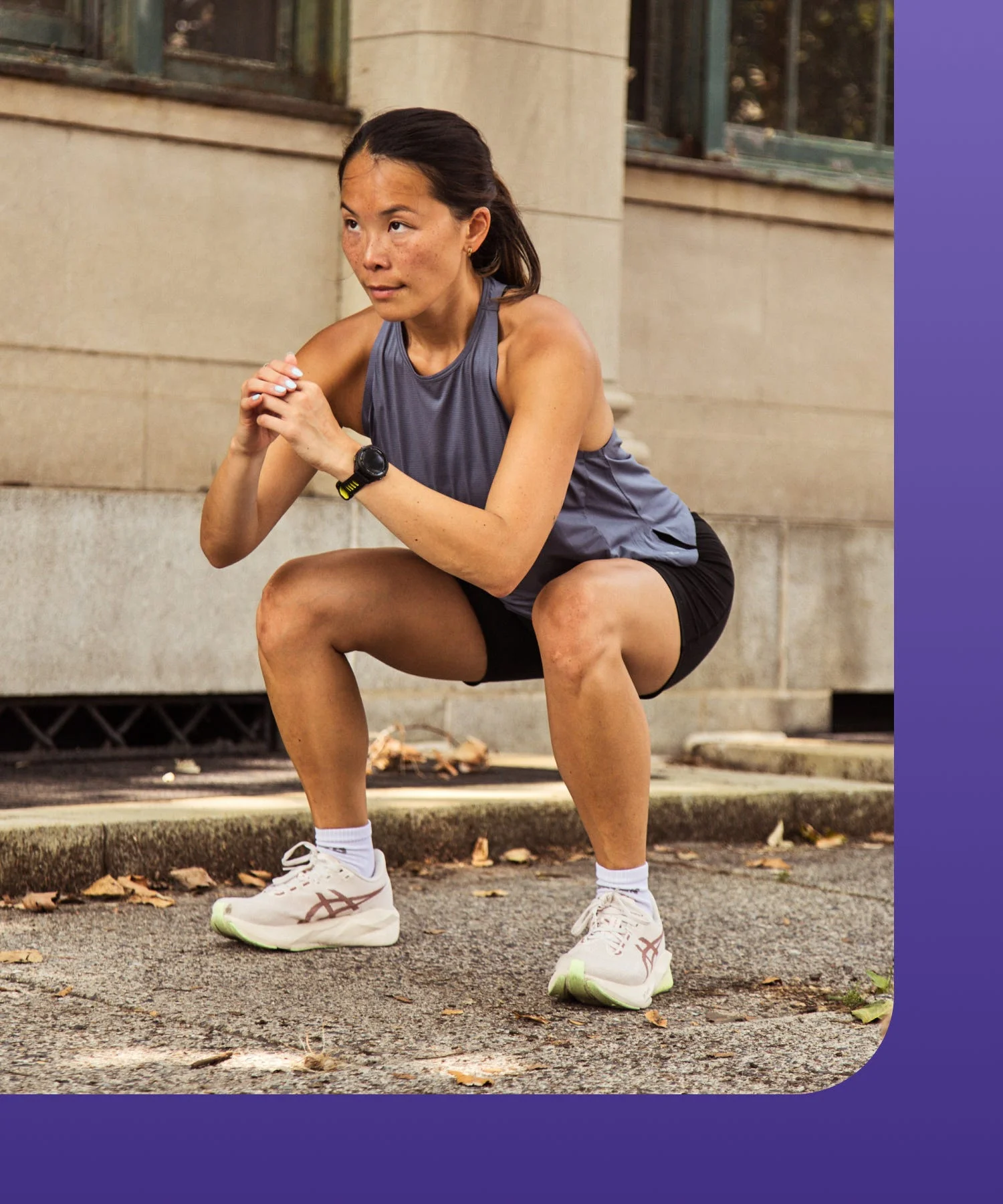A woman performing a squat exercise outdoors on a paved surface.