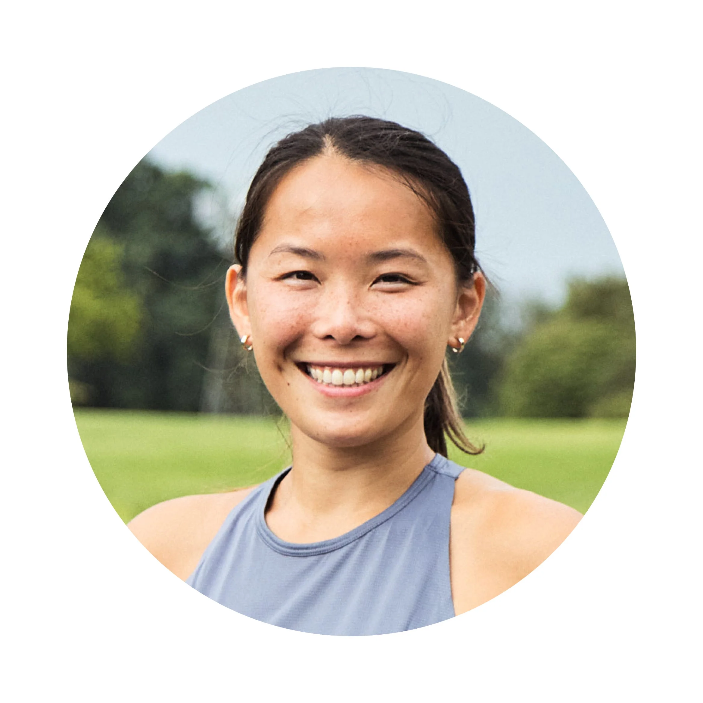 winnie yu, Smiling woman with long hair in a gray top, outdoors in a grassy area.