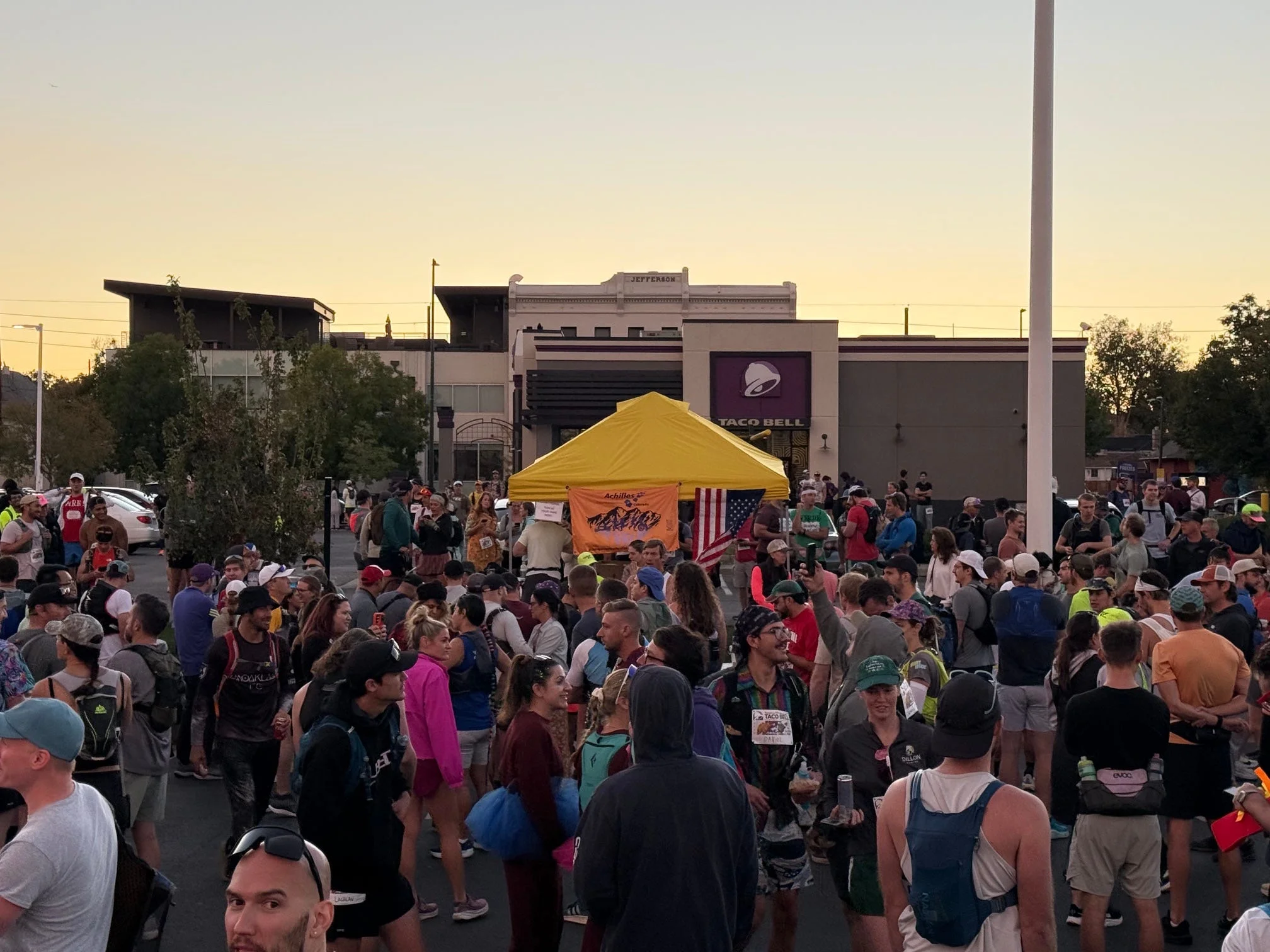 A large crowd gathered around a yellow tent and a Taco Bell during an outdoor event at sunset.