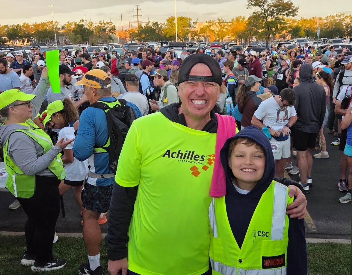 Two smiling individuals in bright vests among a crowd at an outdoor event, showcasing camaraderie and excitement.