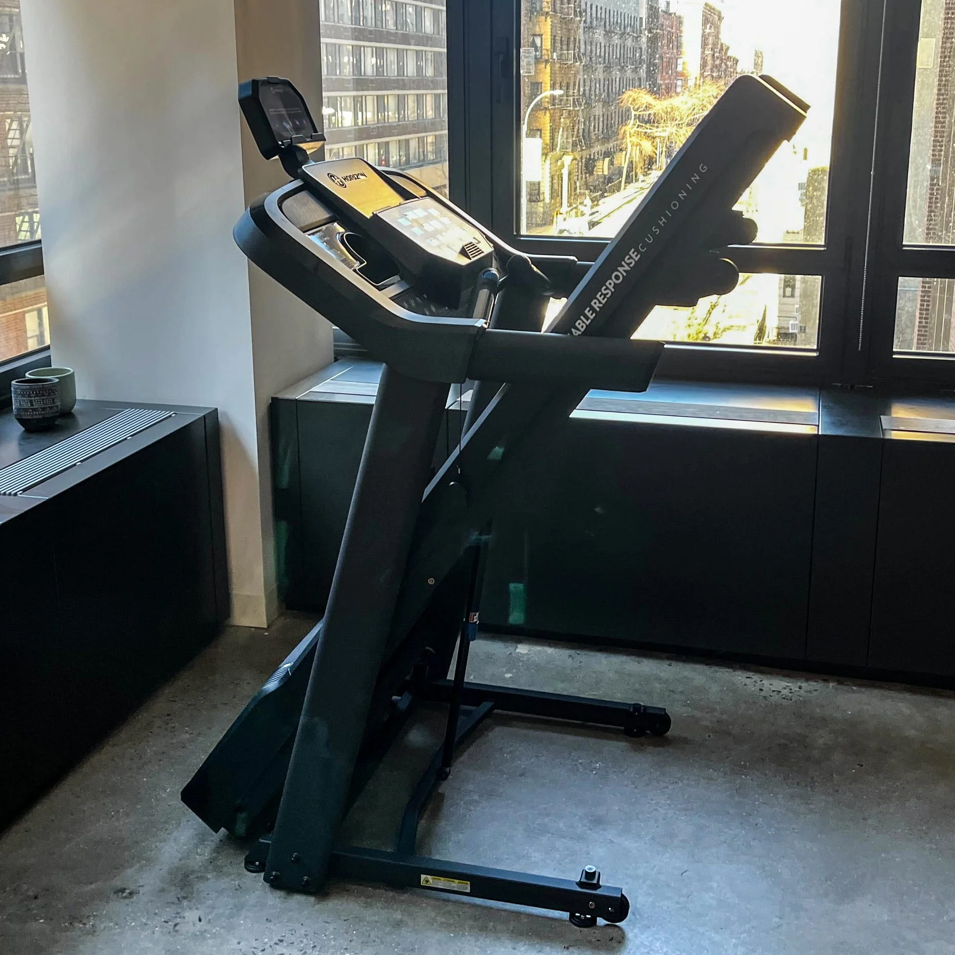 A treadmill positioned next to a large window in an urban setting