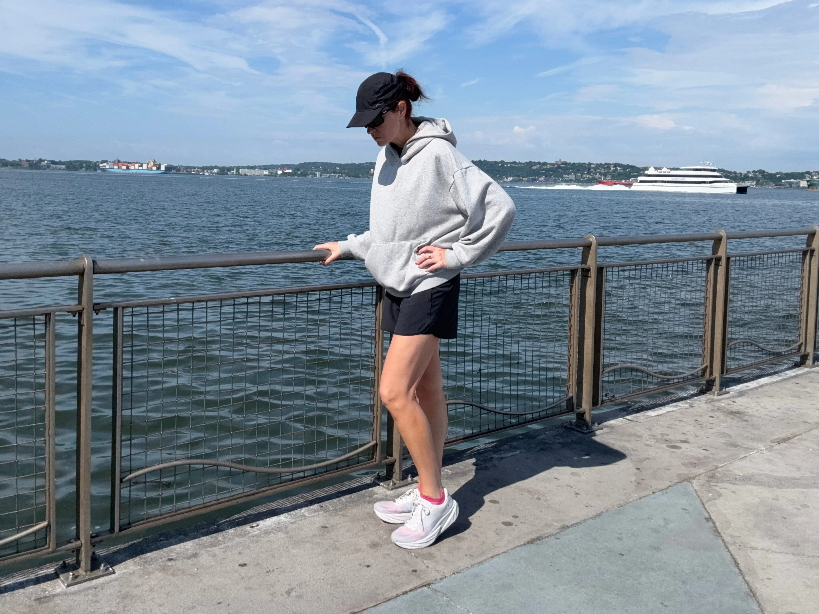 Person in activewear standing by a waterfront railing on a sunny day, sporting New Balance FuelCell Rebel V5
