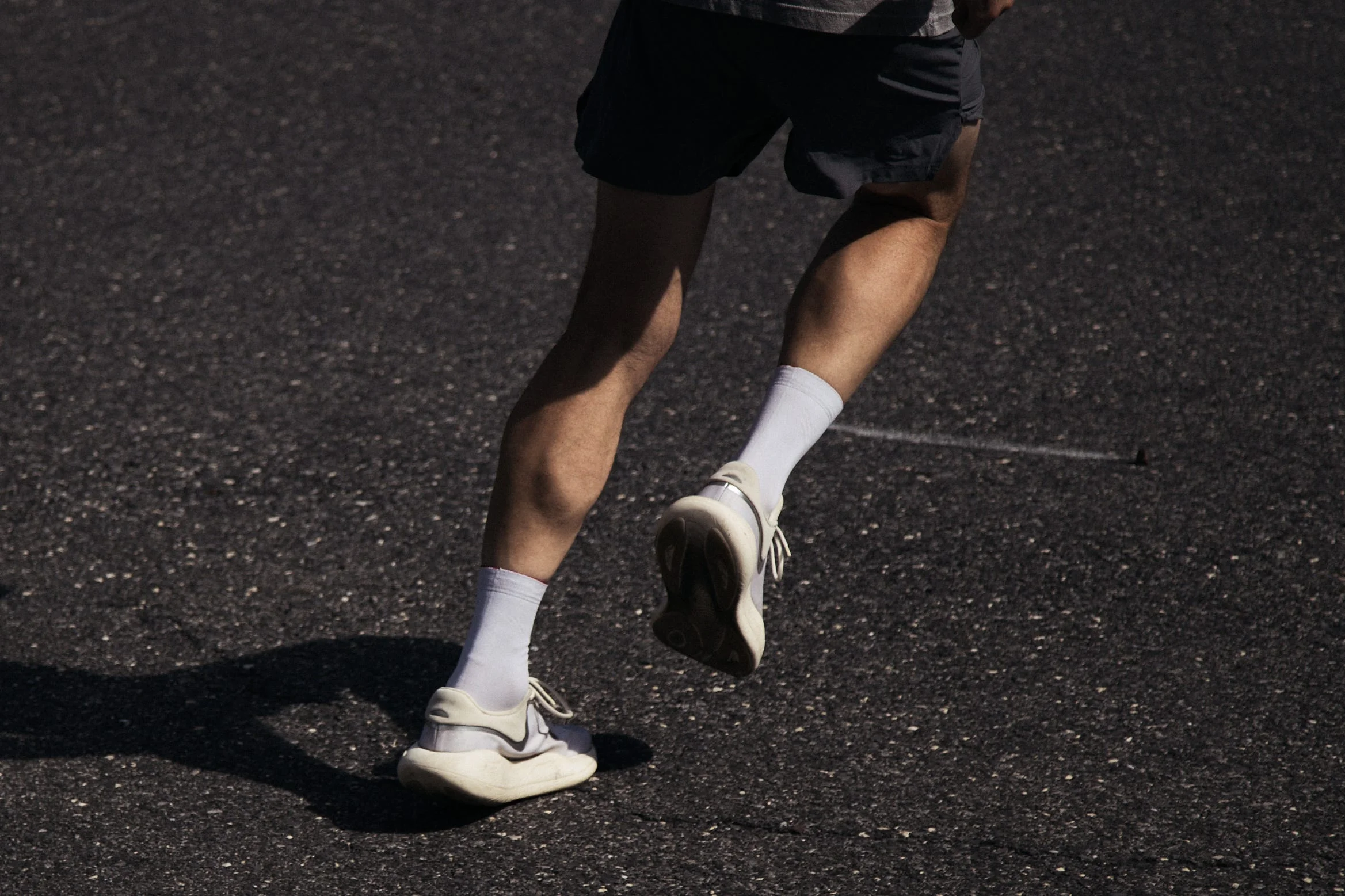 Person running on asphalt in shorts and white sneakers.