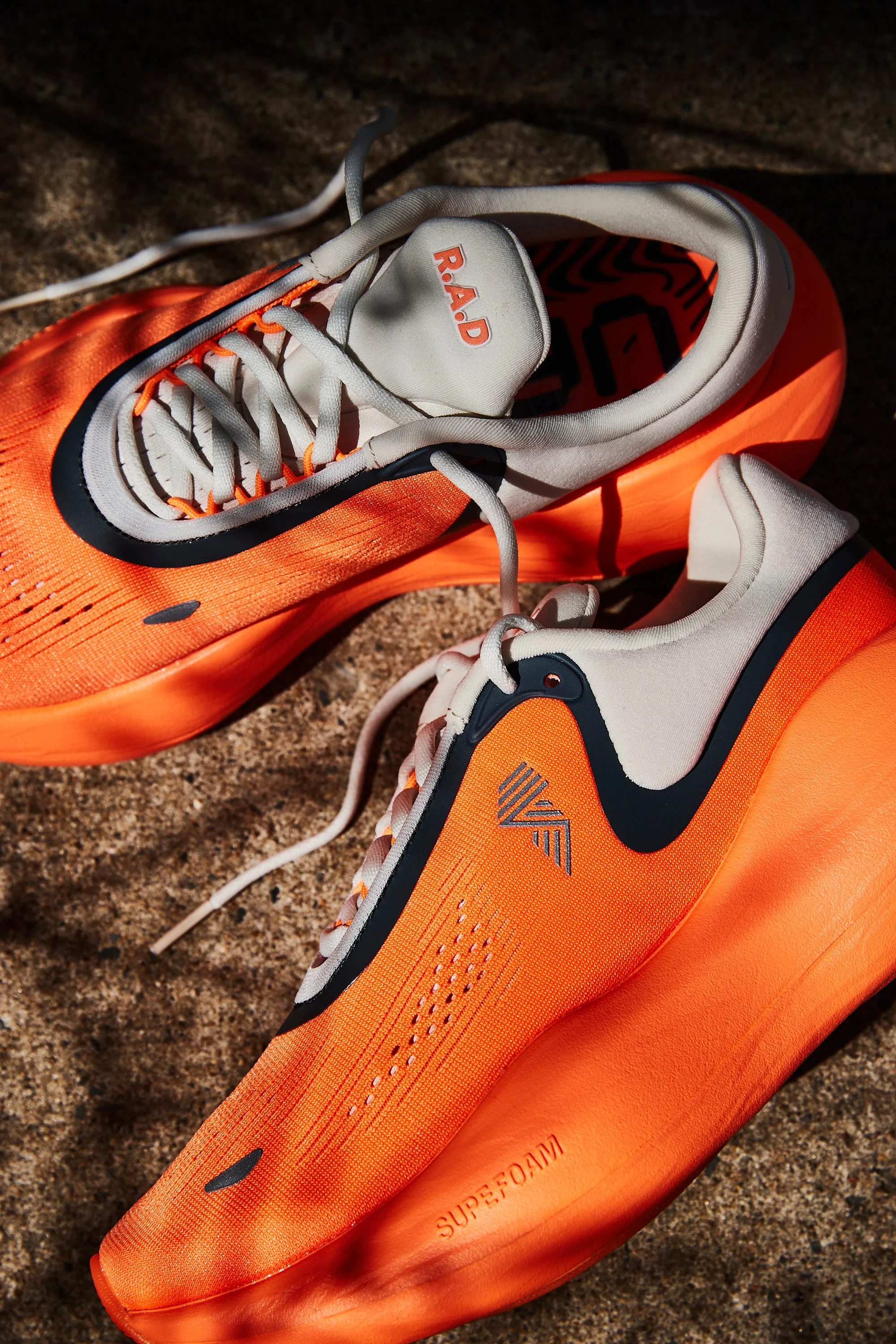 Bright orange running shoes with white and black accents on a stone surface.