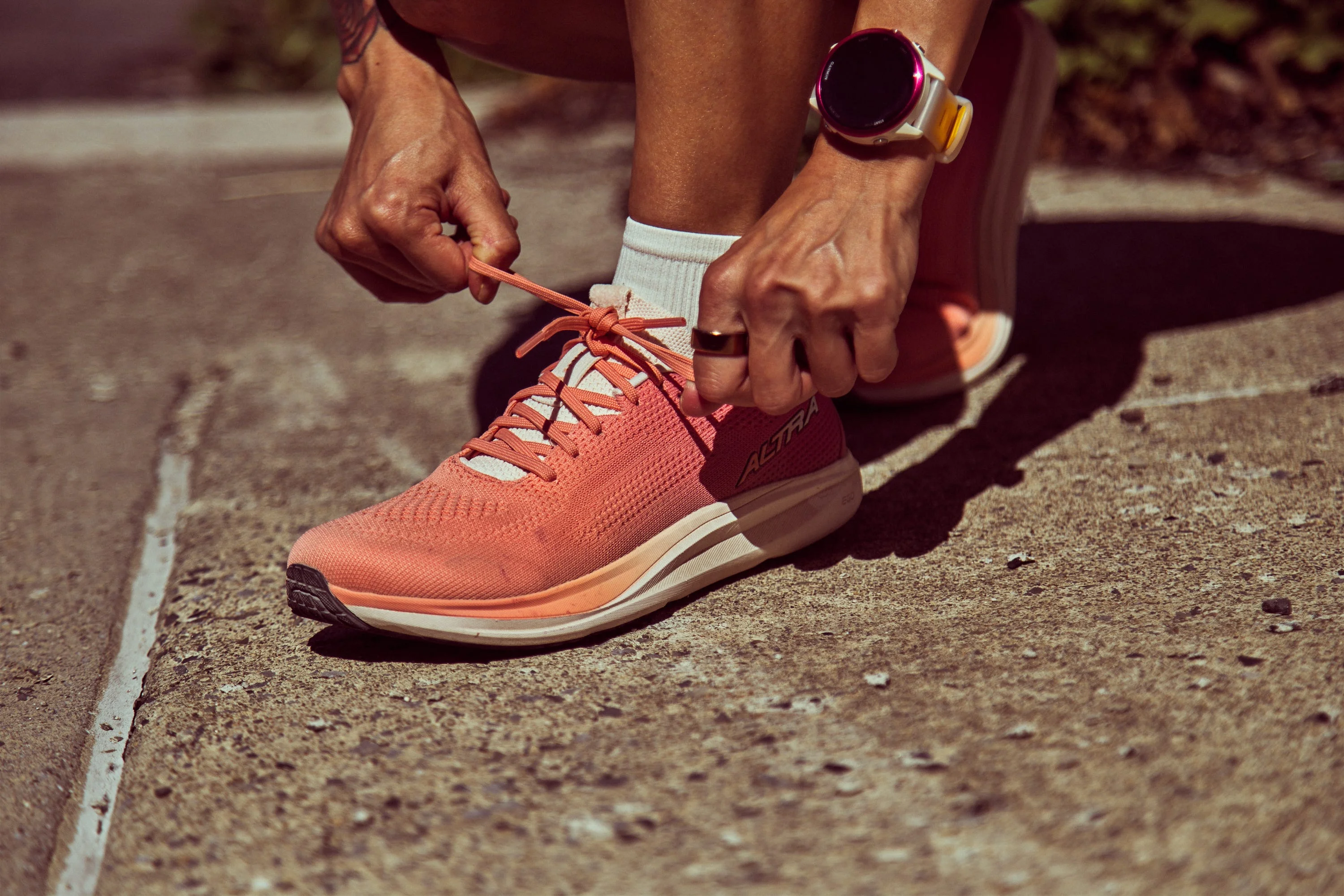 Person tying laces on a pair of bright pink athletic shoes while wearing a smartwatch.