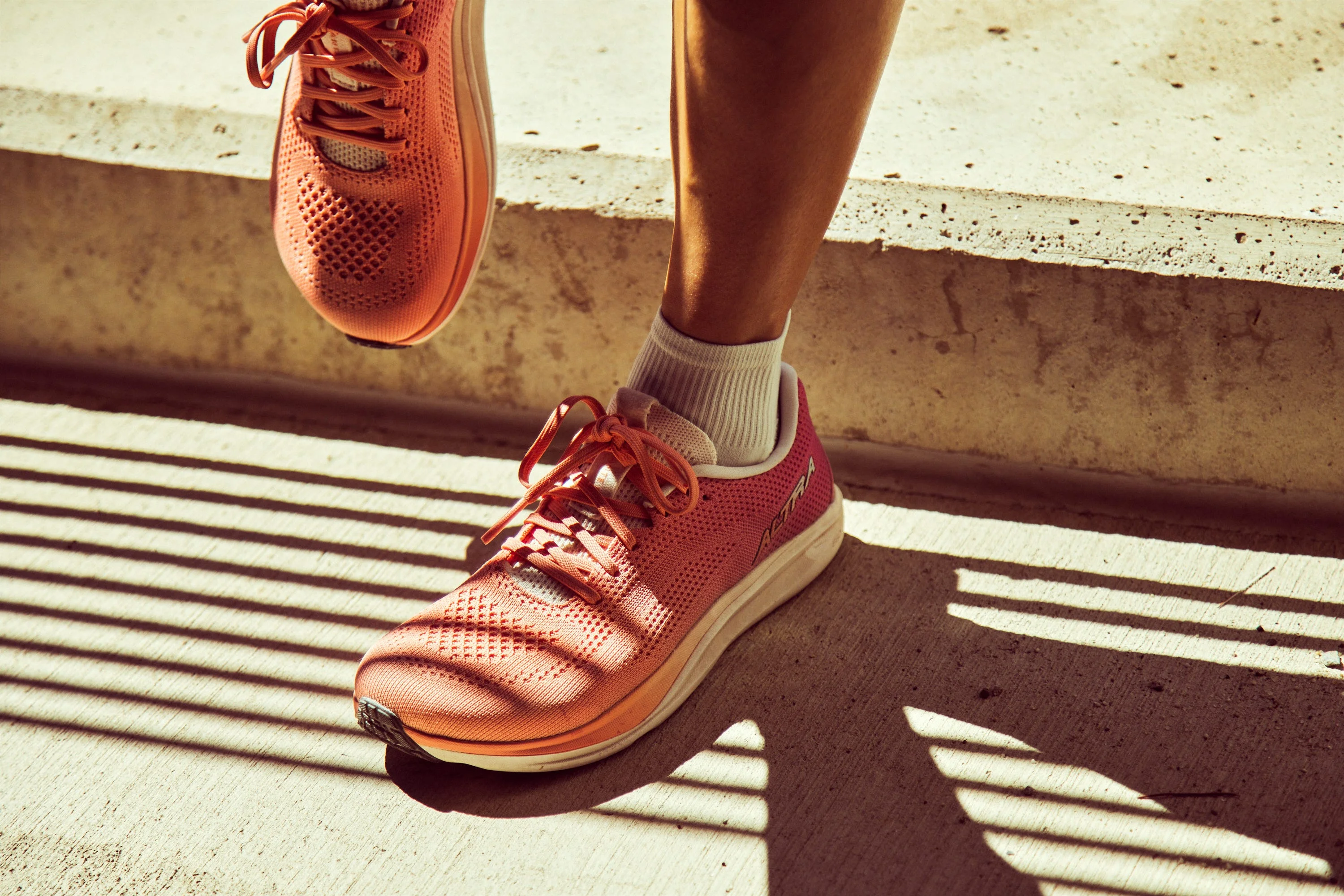 Close-up of a person's foot wearing bright pink running shoes on a concrete surface with shadows.