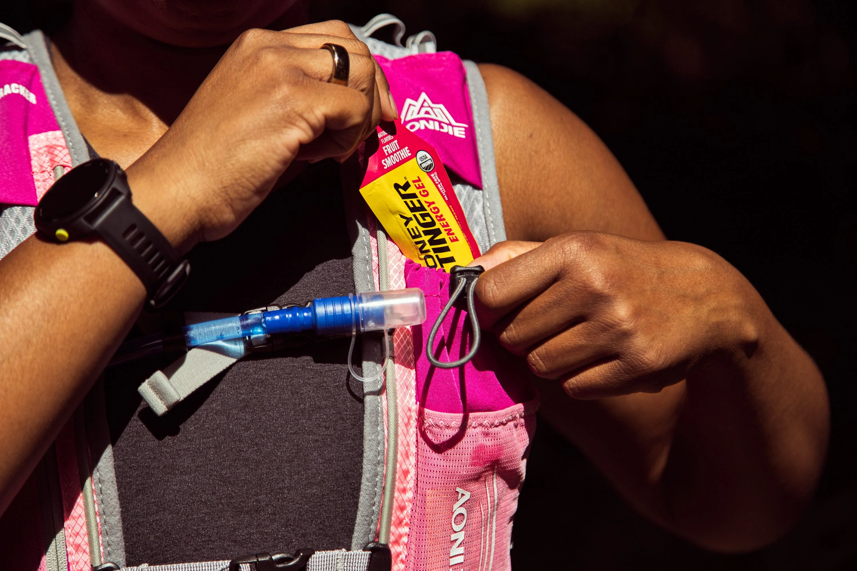 A person inserting an energy gel packet into a hydration vest during outdoor activity A person inserting an energy gel packet into a hydration vest during outdoor activity