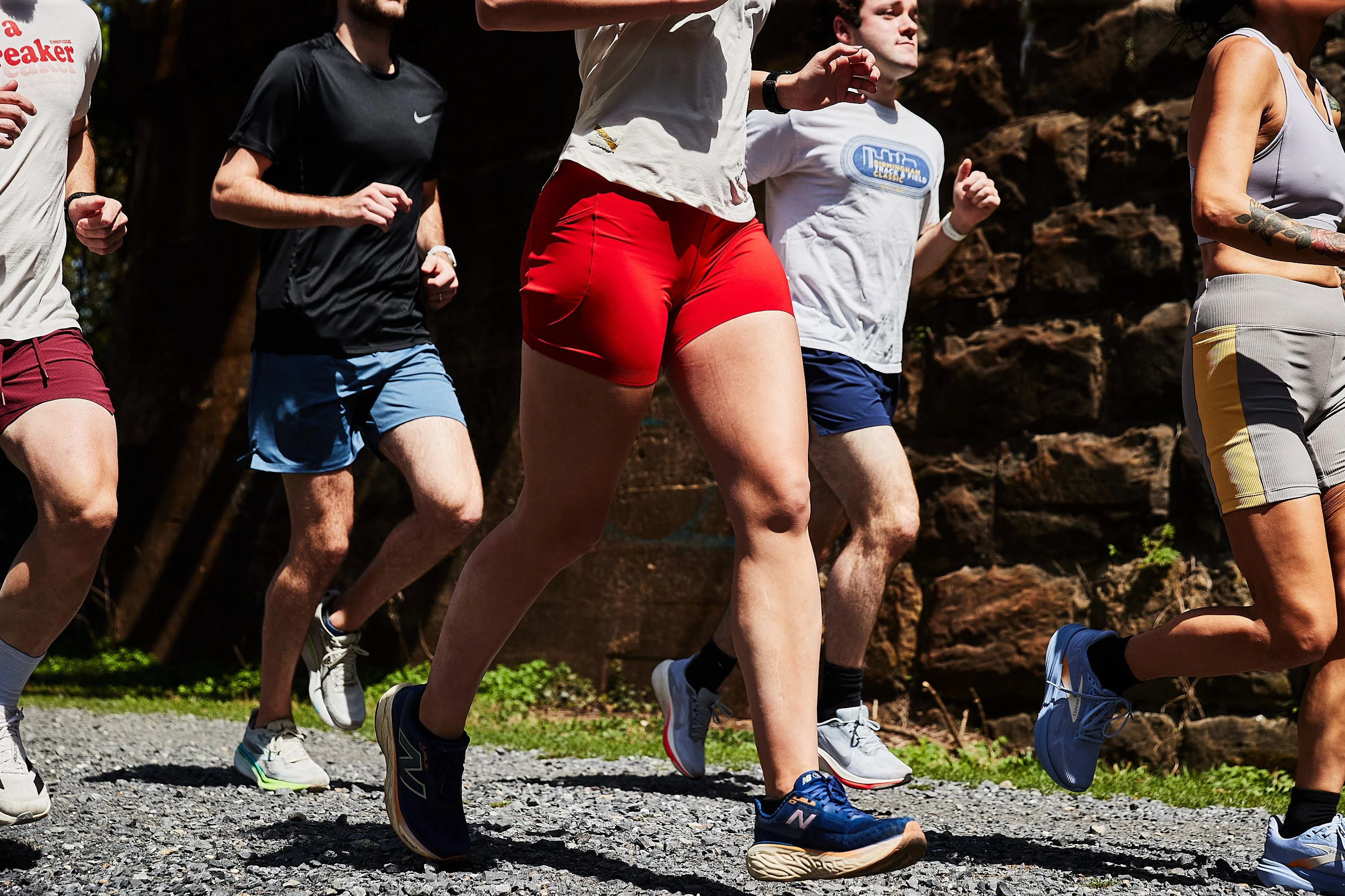 Group of runners in athletic gear jog along a gravel path.
